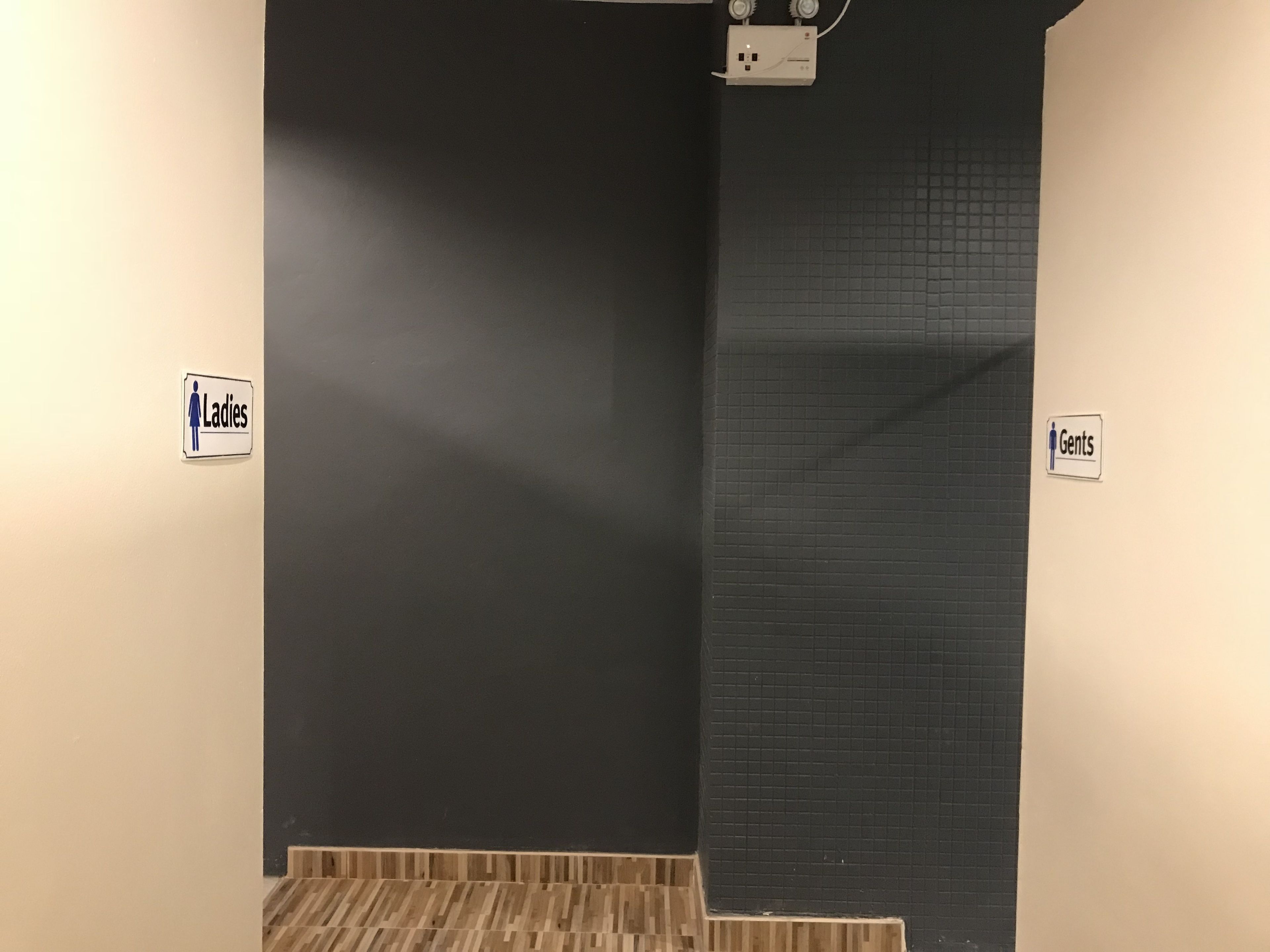 A restroom with a black wall and a tiled section. There are signs indicating 'Ladies' and 'Gents' sections.