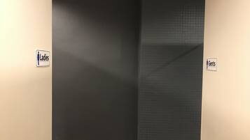 A restroom with a black wall and a tiled section. There are signs indicating 'Ladies' and 'Gents' sections.