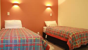 Two single beds with patterned bedding, a wall-mounted light fixture, and a power outlet on the wall.