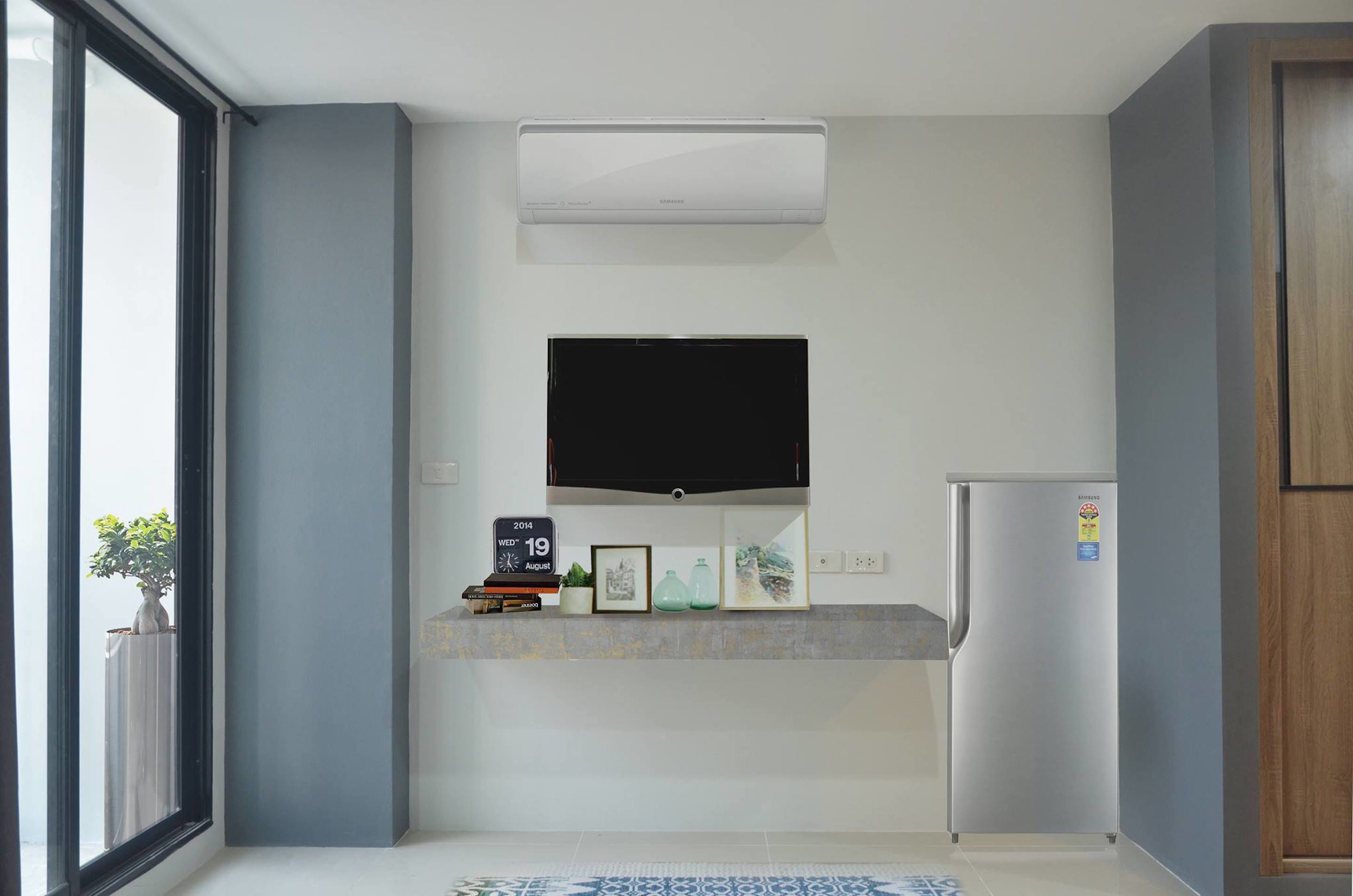 A modern kitchen with a built-in air conditioner, a flat-screen TV, a refrigerator, and a small countertop with decorative items.
