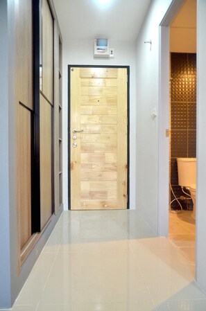 A hallway with a wooden door, a tiled floor, and a bathroom visible to the right. - At Yaya (Bangkok)
