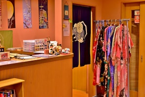 A reception area with a wooden counter, various decorative items, and a clothing rack with colorful garments. - Ryokan Shimizu (Kyoto)