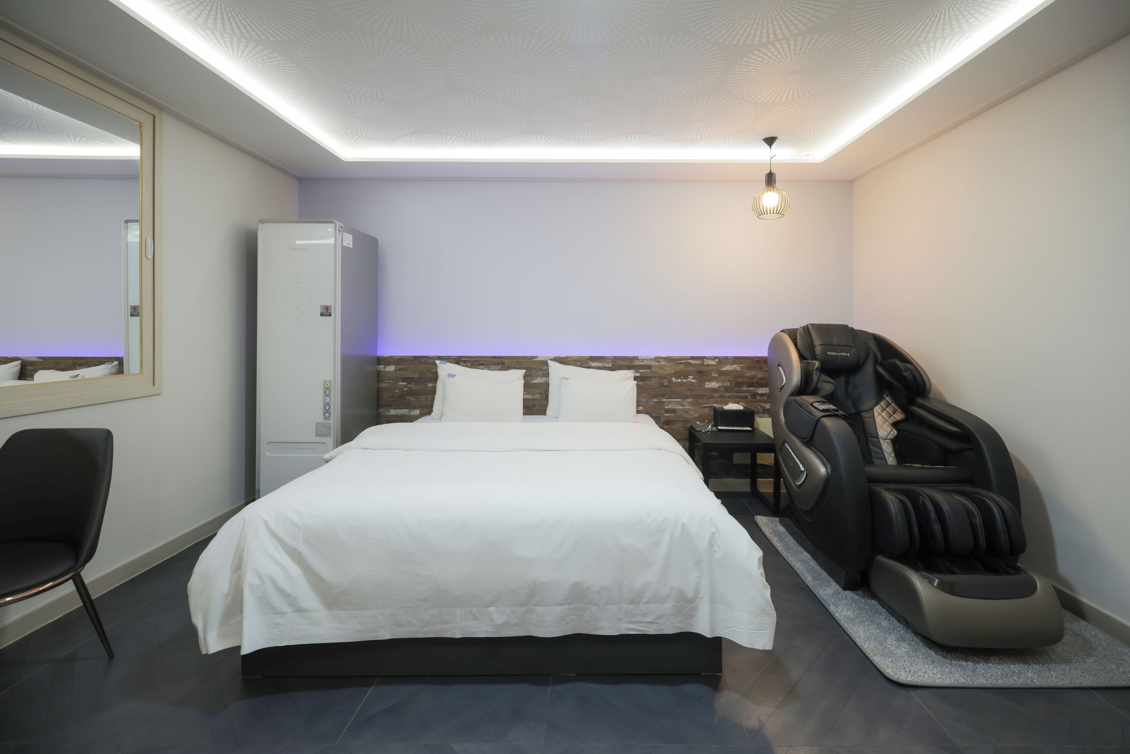 Un dormitorio moderno con una cama grande, una silla de masaje, un armario y un espejo.