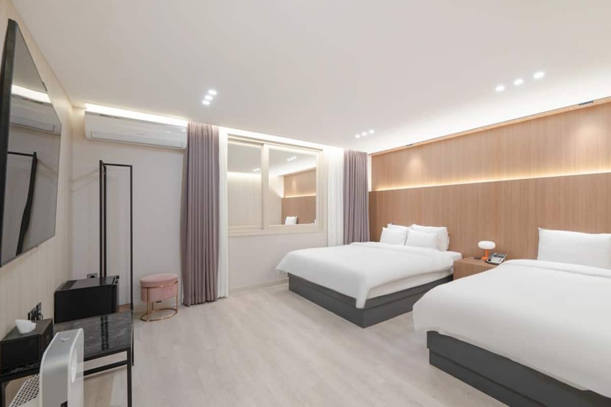 Habitación de hotel con dos camas, un escritorio, un espejo, un televisor y una ventana con cortinas.