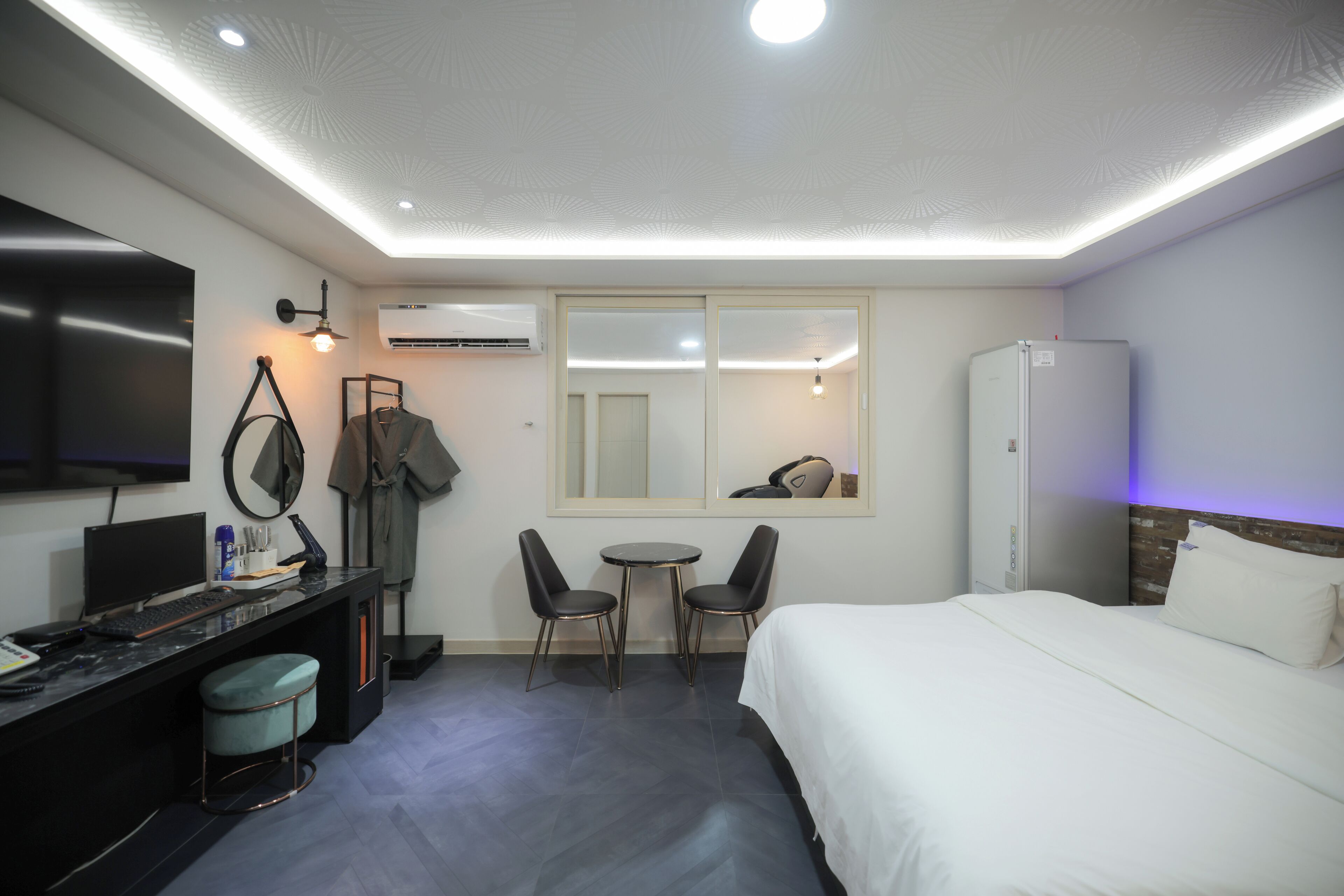 A hotel room with a bed, desk, chairs, a TV, and a refrigerator.
