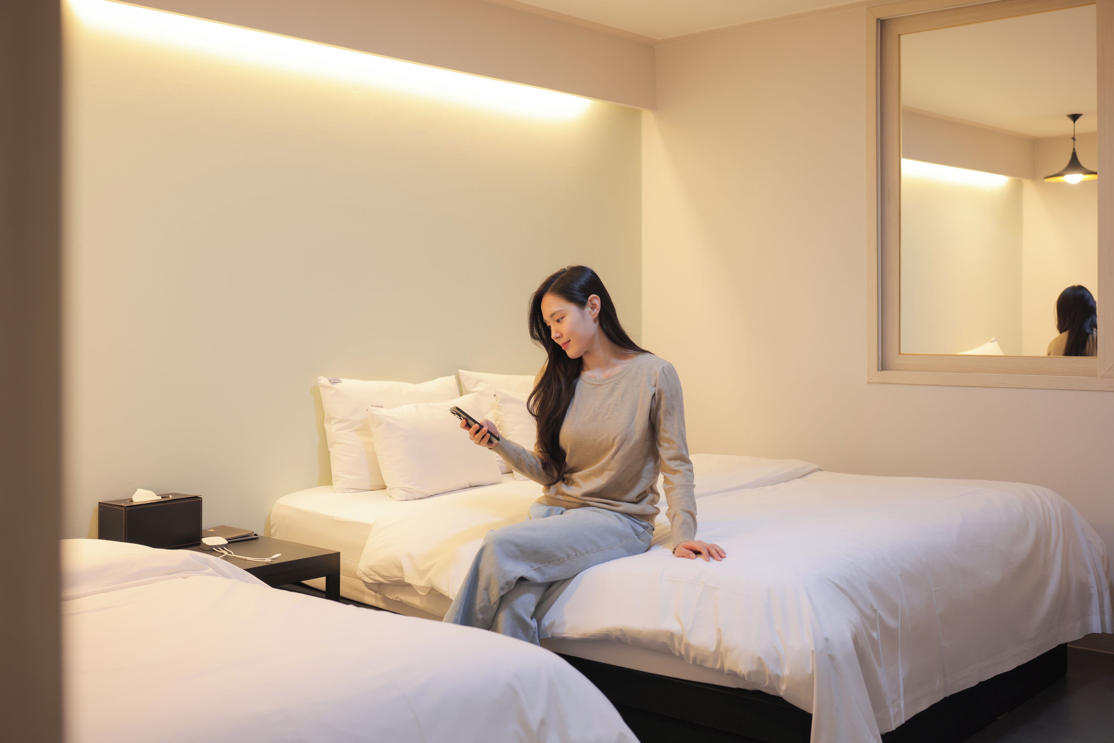 A hotel room with two beds, a bedside table with a lamp, and a large mirror on the wall.