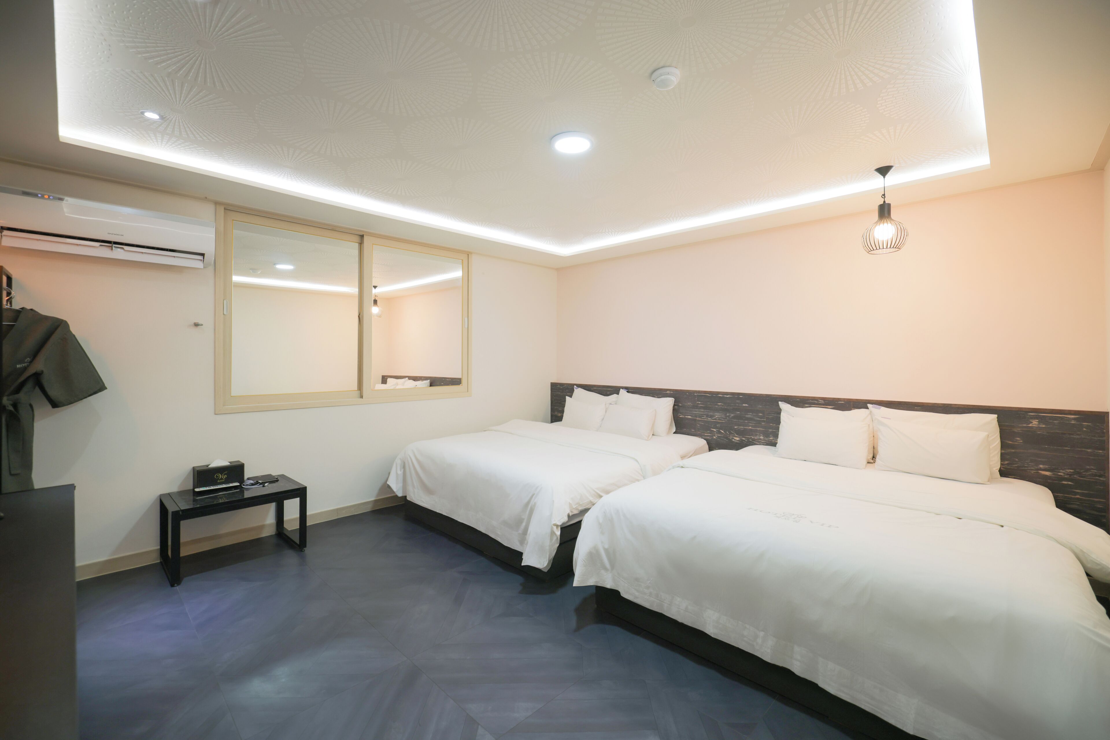Una habitación de hotel moderna con dos camas, una mesita, un espejo y una lámpara en el techo.