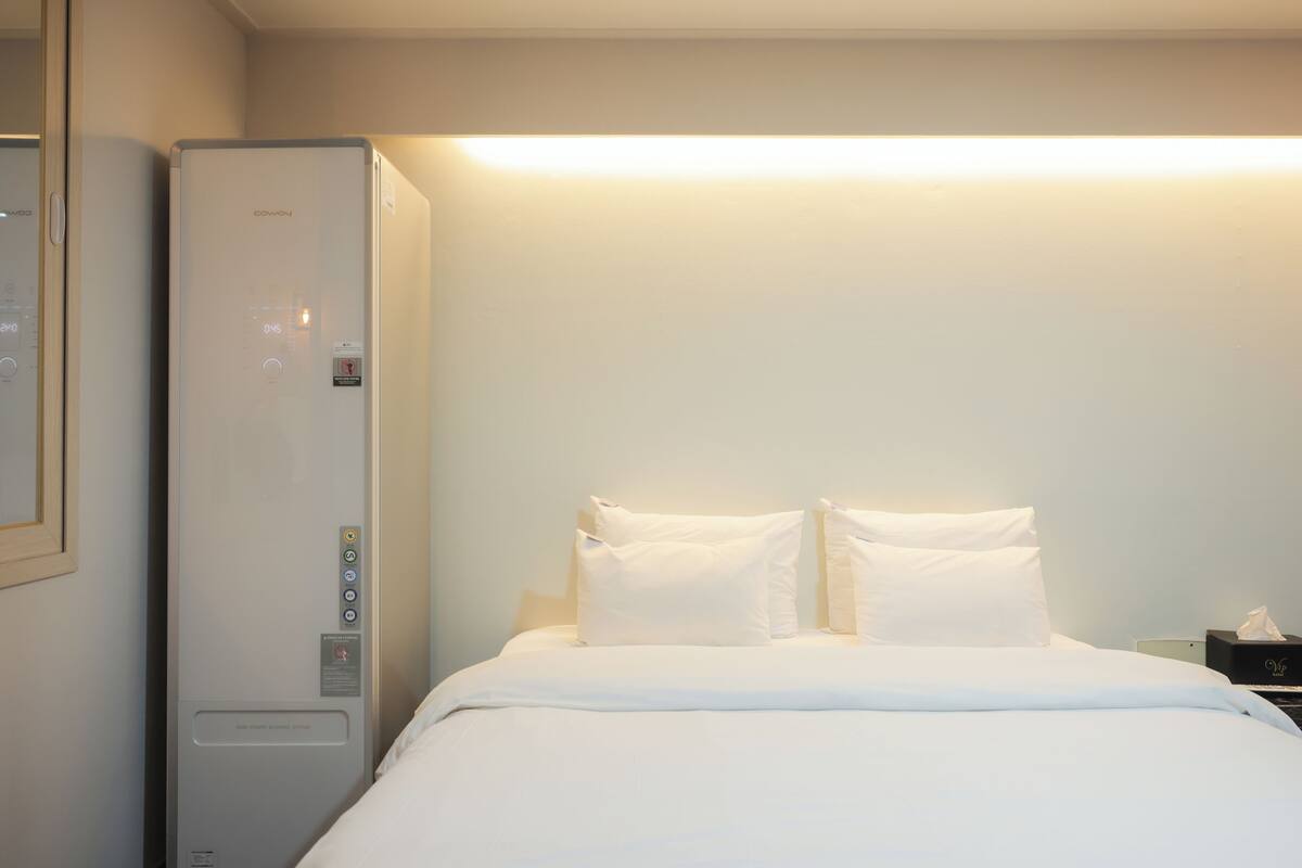 Habitación de hotel con cama, ropa de cama blanca, una mesita de noche, una lámpara y un calentador de pared.
