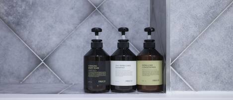 Three bottles of Freco body wash and conditioner on a shelf against a tiled wall.