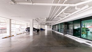 A spacious indoor parking area with a clean, modern design, featuring a polished concrete floor and white ceiling pipes. - Ruan Plaisoi Apartment by Zuzu (Bangkok)