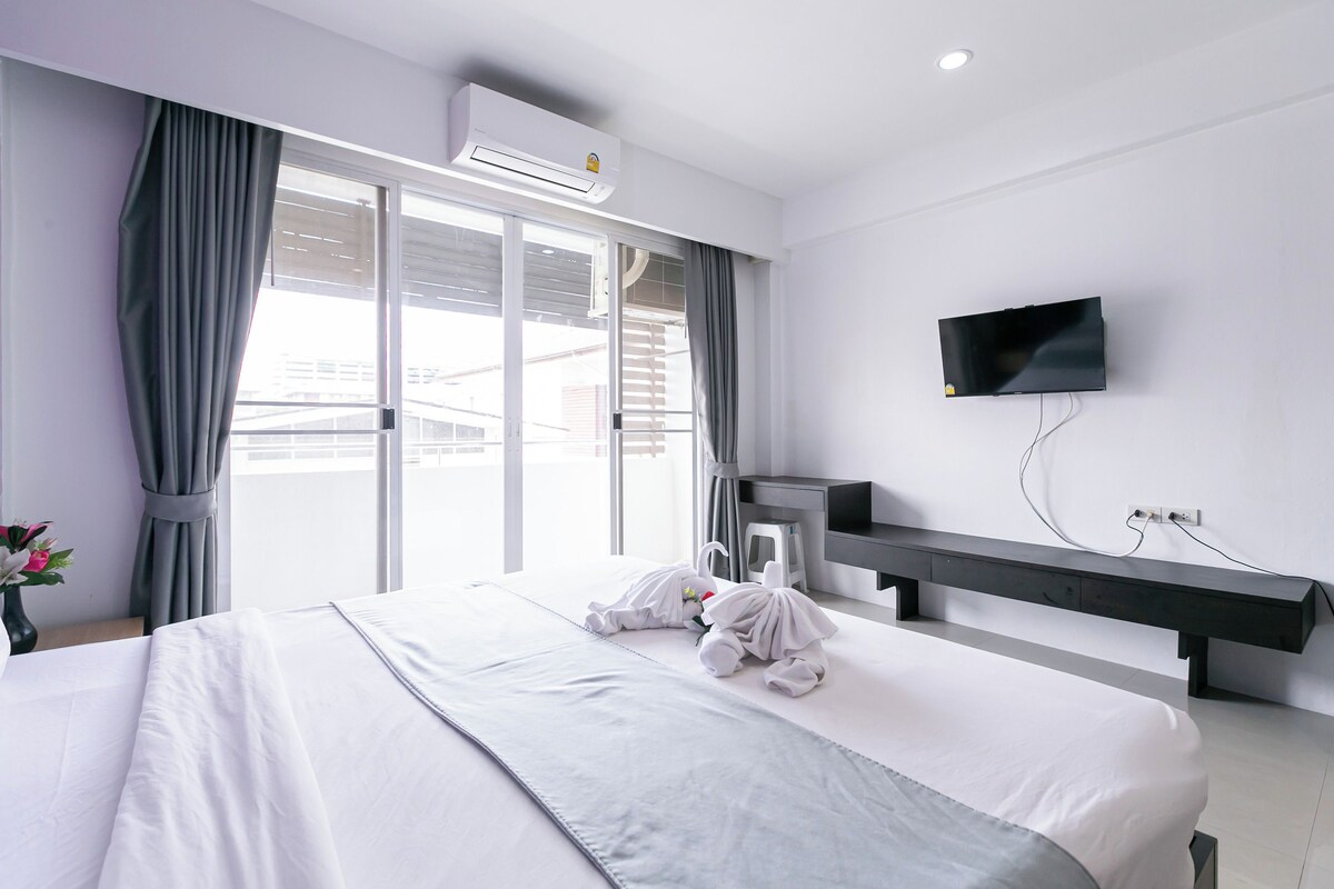 A hotel room with a bed, a TV mounted on the wall, and a window with curtains.