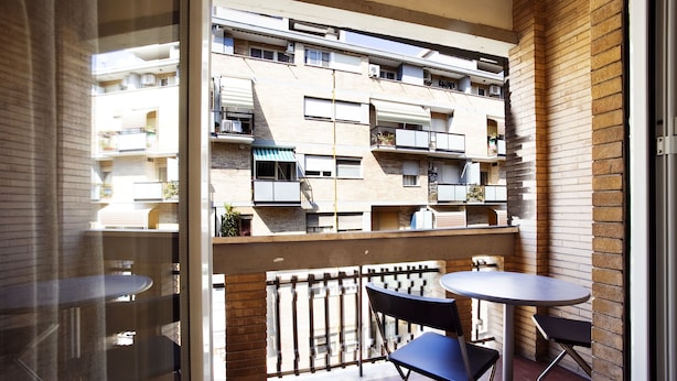 Een balkon met uitzicht op een meerhoog gebouw, een tafel en twee stoelen.