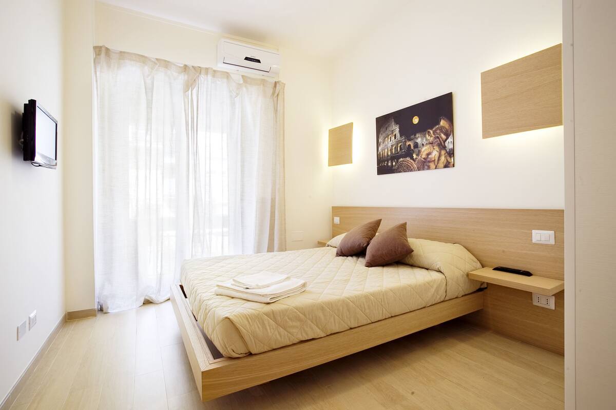 Un dormitorio con cama, cortinas, un cuadro, una mesita de noche y un aire acondicionado de pared.