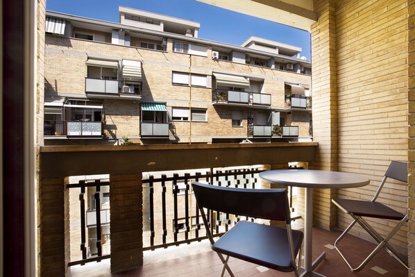 A balcony with a table and chairs, overlooking a multi-story building with balconies.