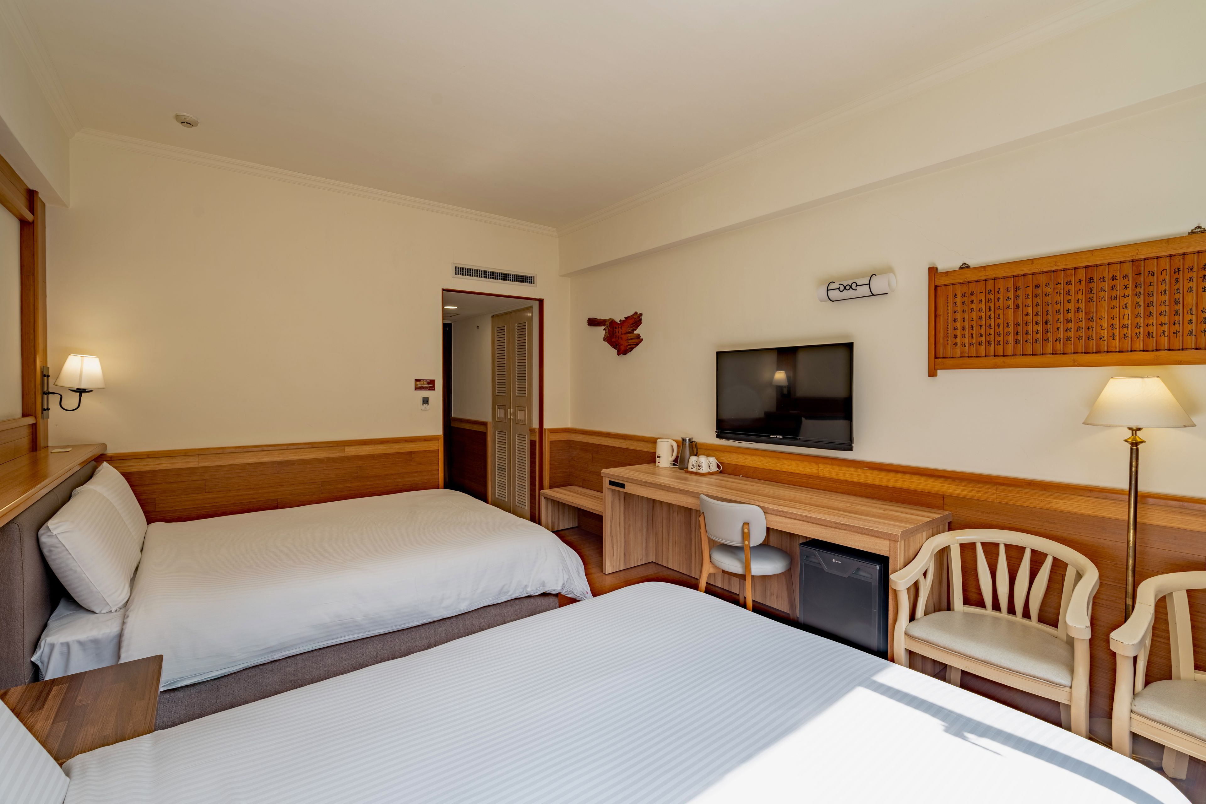Habitación de hotel con dos camas, un escritorio con silla, un televisor y una obra de arte colgada en la pared.