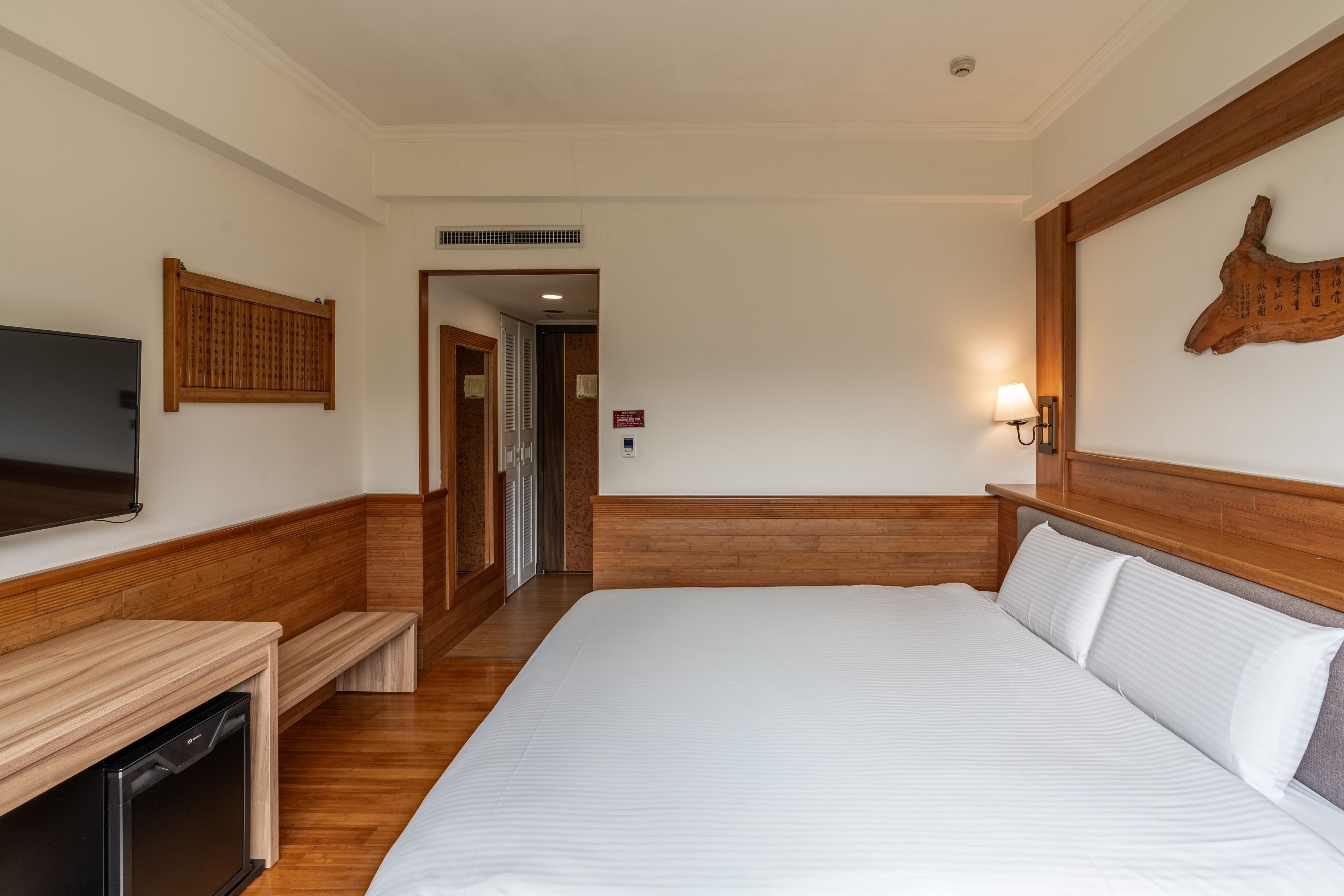 Ein Hotelzimmer mit einem großen Bett, einem Flachbildfernseher, einem Holz-Kopfteil, einem angebrachten Fernseher, einer wandmontierten Lampe und einem Holzboden.