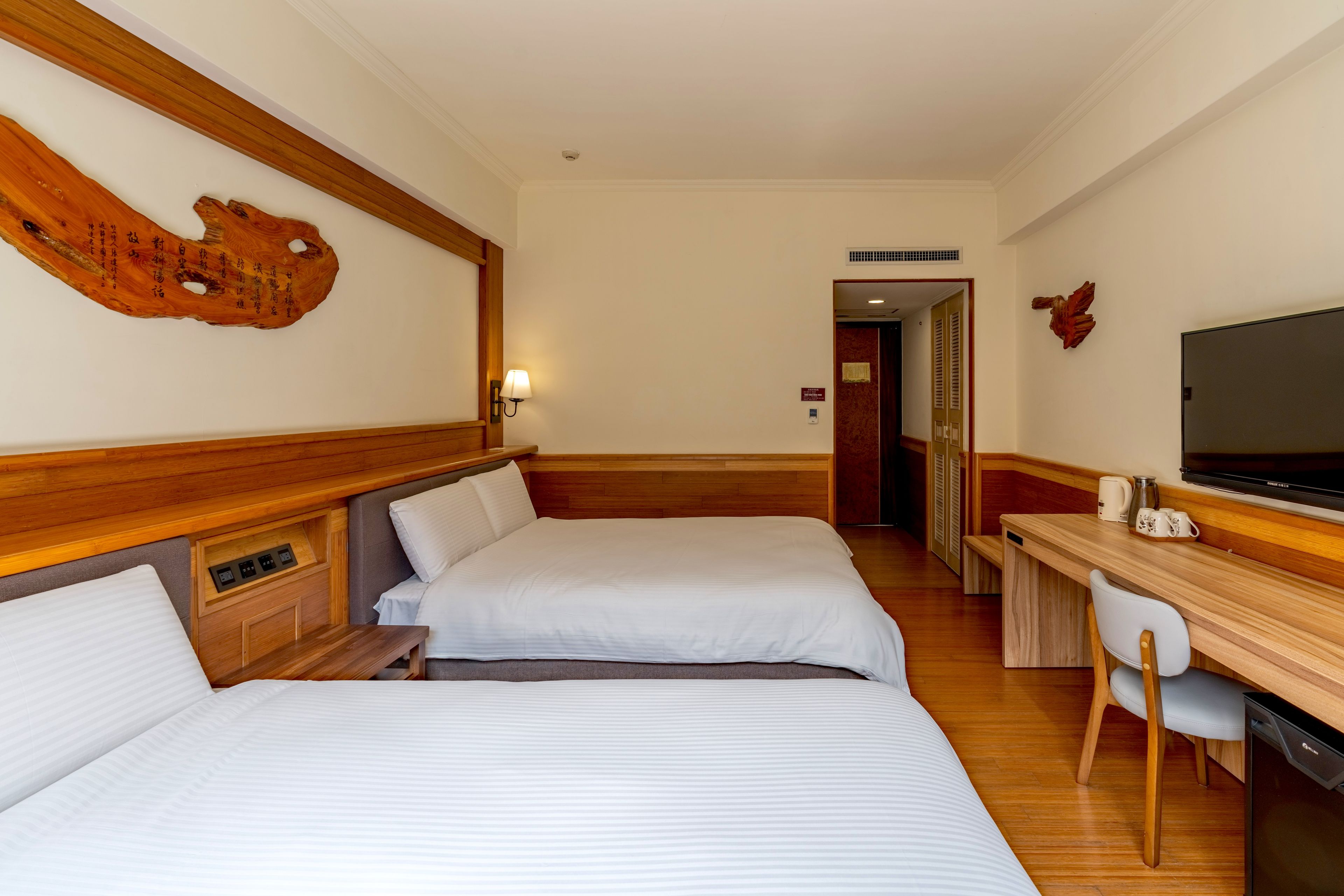 Habitación de hotel con dos camas, un escritorio, una silla, un televisor y una pared decorativa de madera.