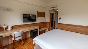 A hotel room with a bed, a desk with a chair, a television, and a wardrobe. - Ginkgo Hotel (Lugu)