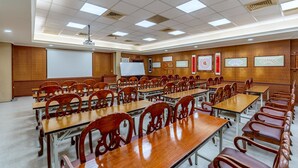 Un salón de conferencias con varias mesas y sillas, una pizarra blanca y caligrafía enmarcadas en las paredes.