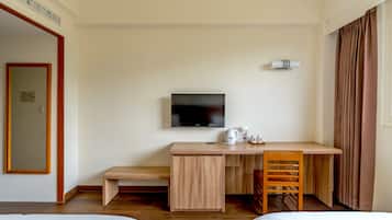A hotel room with a wooden desk, a television, a bed, and a window with curtains.