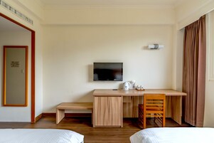 Une chambre d’hôtel avec un bureau en bois, une télévision, un lit et une fenêtre avec des rideaux.
