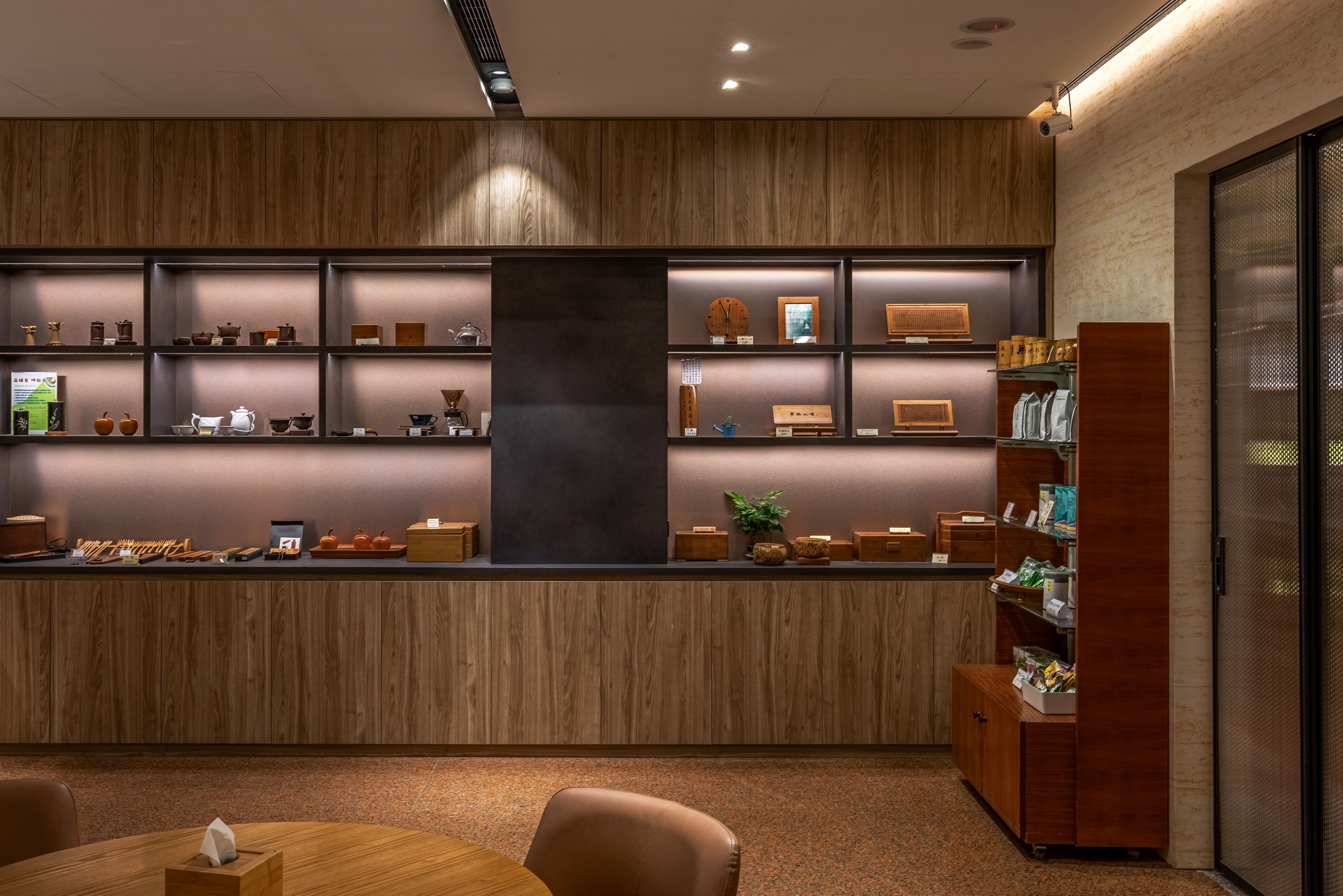 A modern interior with a wooden reception desk, shelves with various items, and a seating area with a table and chairs.