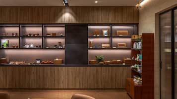 A modern interior with a wooden reception desk, shelves with various items, and a seating area with a table and chairs.