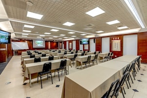 Un salón de conferencias con varias mesas y sillas, una pantalla de proyector y un televisor.