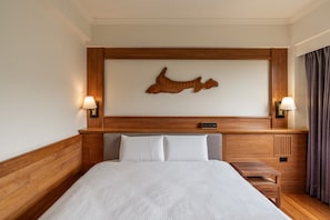 Une chambre d’hôtel comprenant un lit, deux lampes de chevet, une tête de lit en bois, une œuvre d’art accrochée au mur et une table de chevet.
