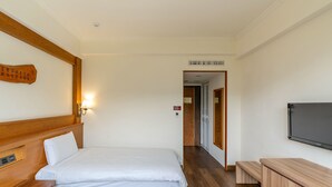 Habitación de hotel con dos camas, cabecera de madera, televisor montado en la pared y un banco de madera.