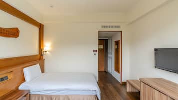 A hotel room with two beds, a wooden headboard, a wall-mounted TV, and a wooden bench.