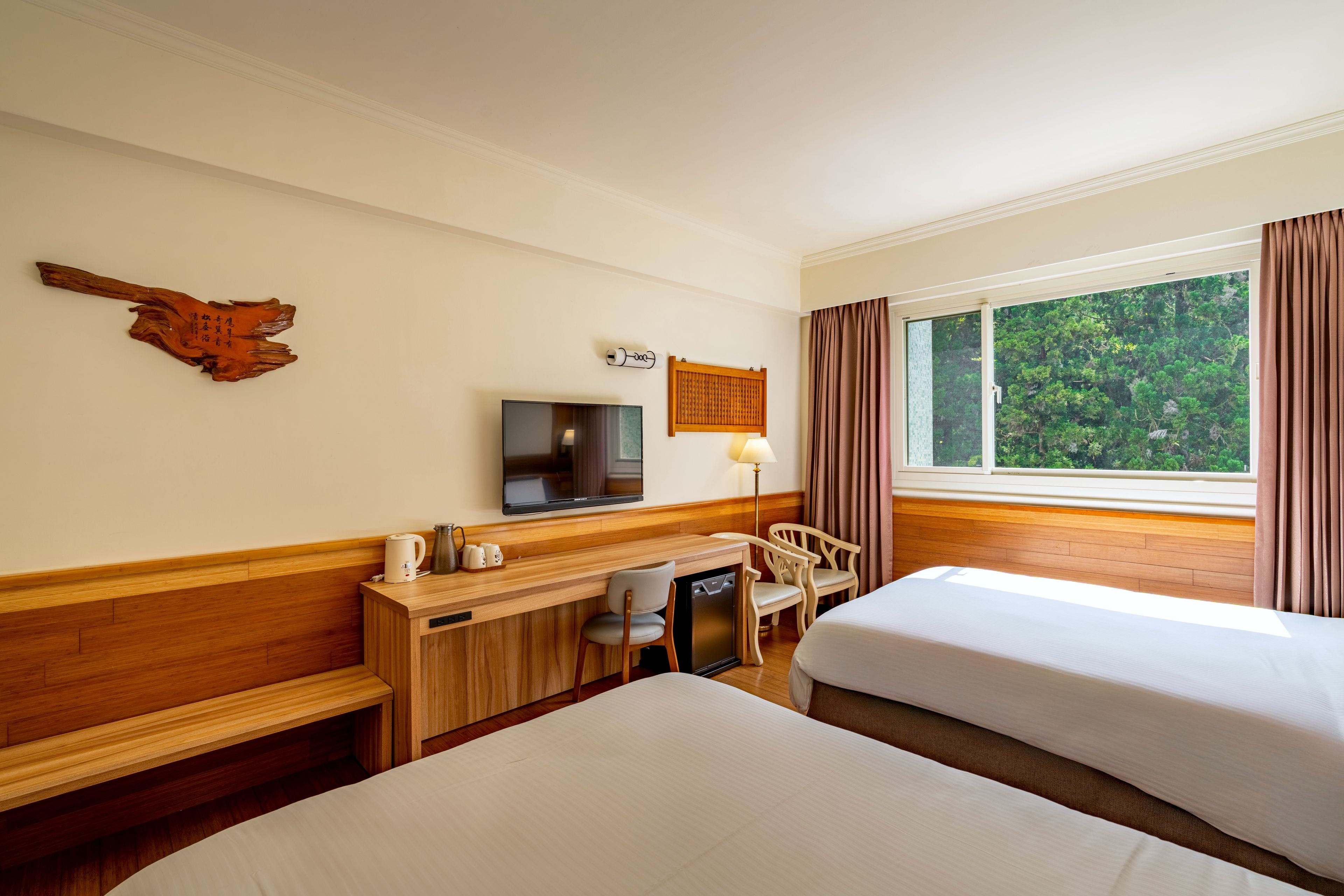 A hotel room with two beds, a desk with a TV, a wooden cabinet, and a window with curtains.