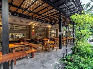 An outdoor cafe with wooden tables and chairs, a covered seating area, and a view of greenery. - Ginkgo Hotel (Lugu)