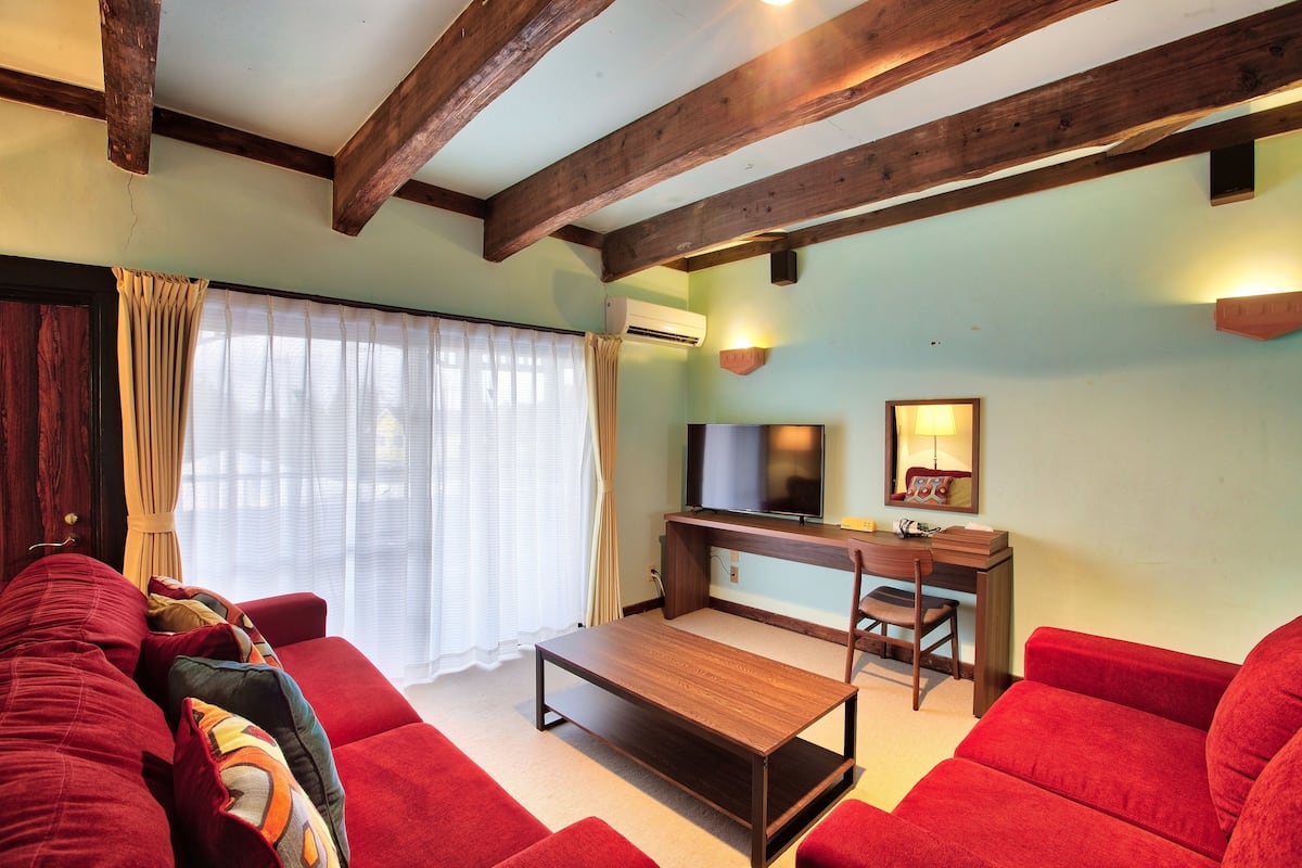 A living room with a red sofa, a wooden coffee table, a TV, and a desk with a chair.