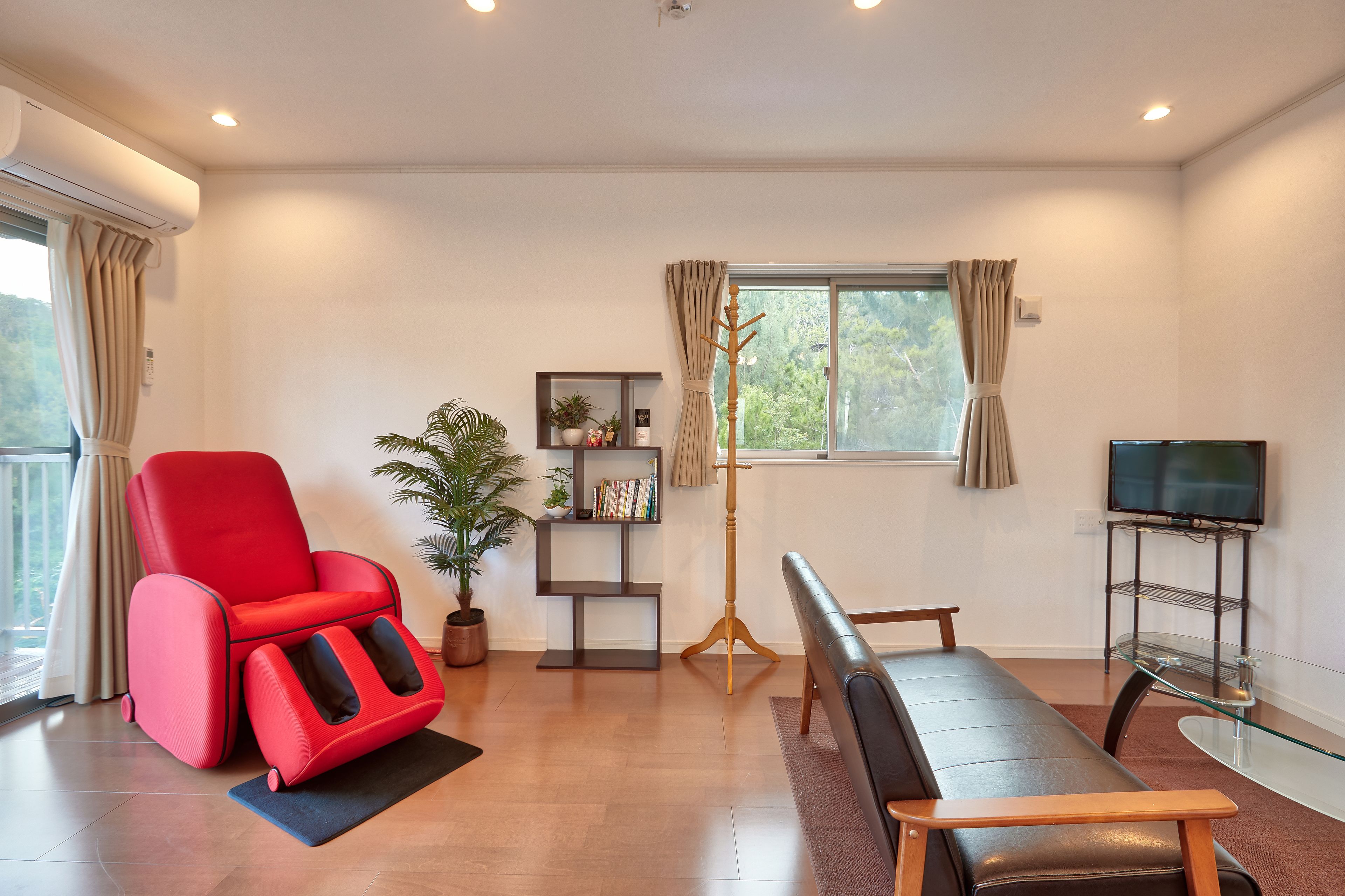 A modern living room with a red recliner, a black sofa, a floor lamp, a bookshelf, and a TV on a stand.