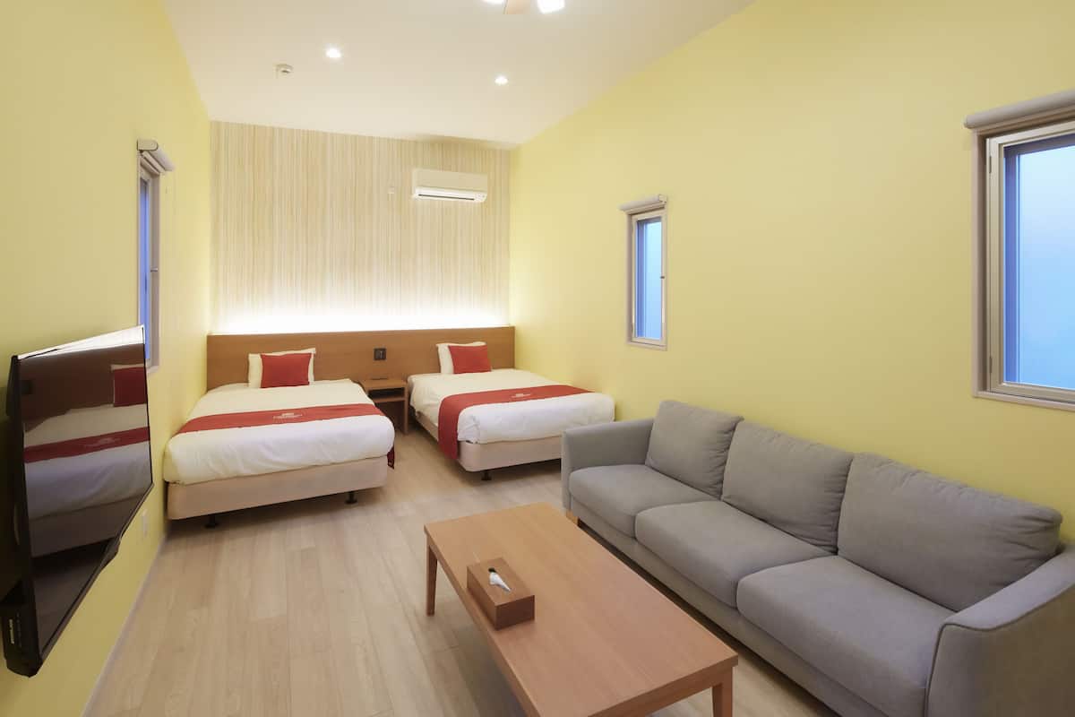 A hotel room with two single beds, a sofa, a TV, and a wooden table.