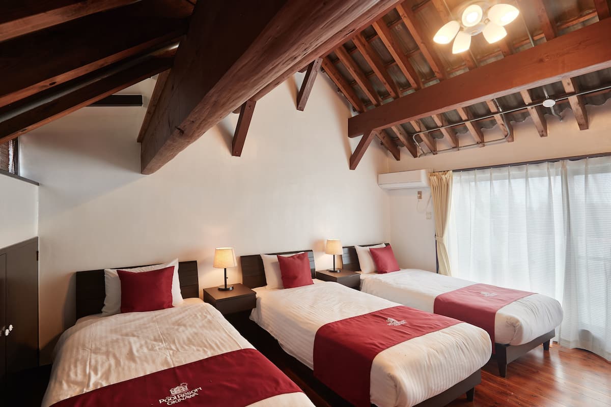 A hotel room with three beds, wooden beams, a ceiling fan, and a window with curtains.