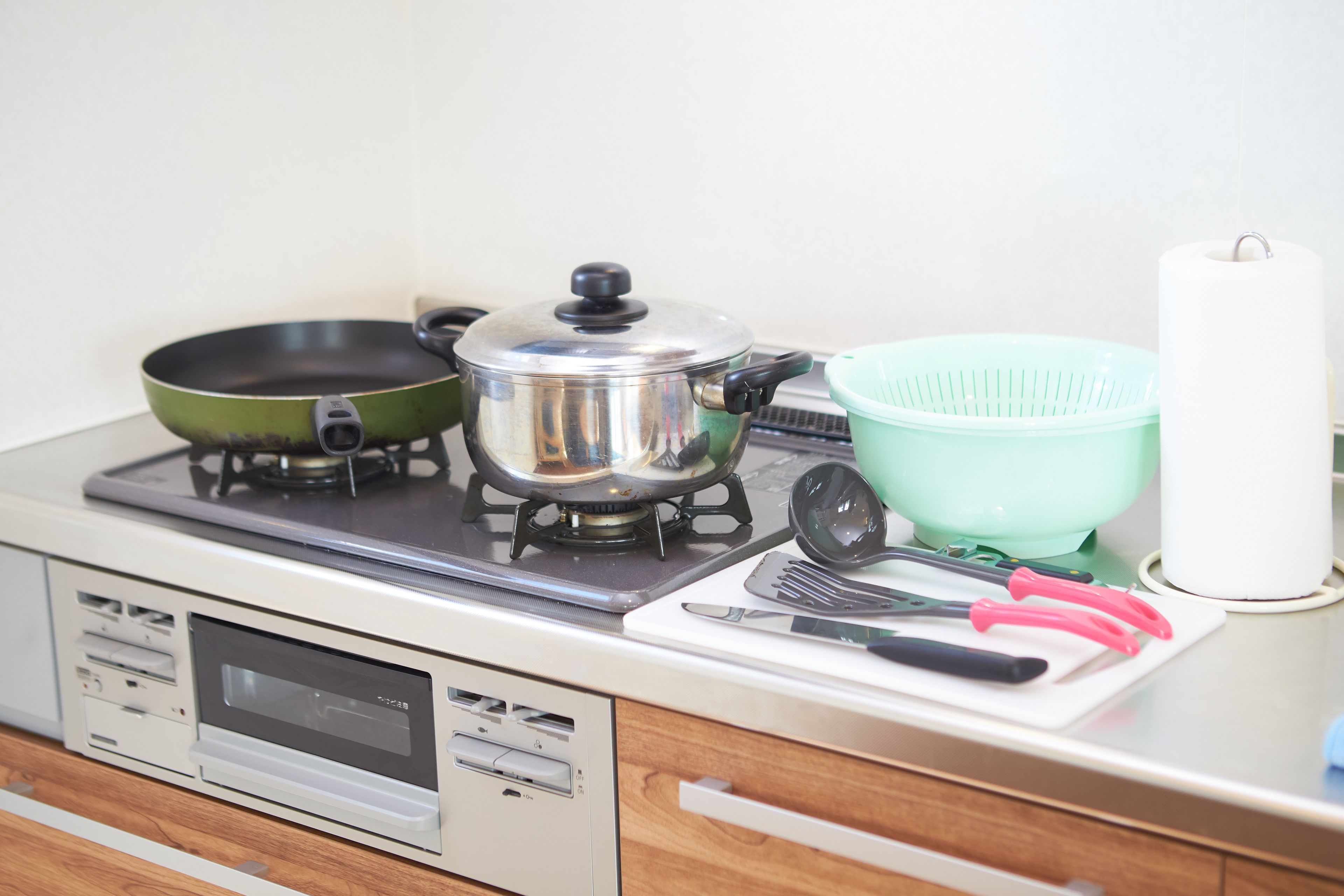 Una cocina con estufa, olla, sartén, colador y varios utensilios.