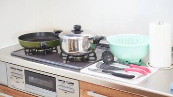 Una cocina con estufa, olla, sartén, colador y varios utensilios.