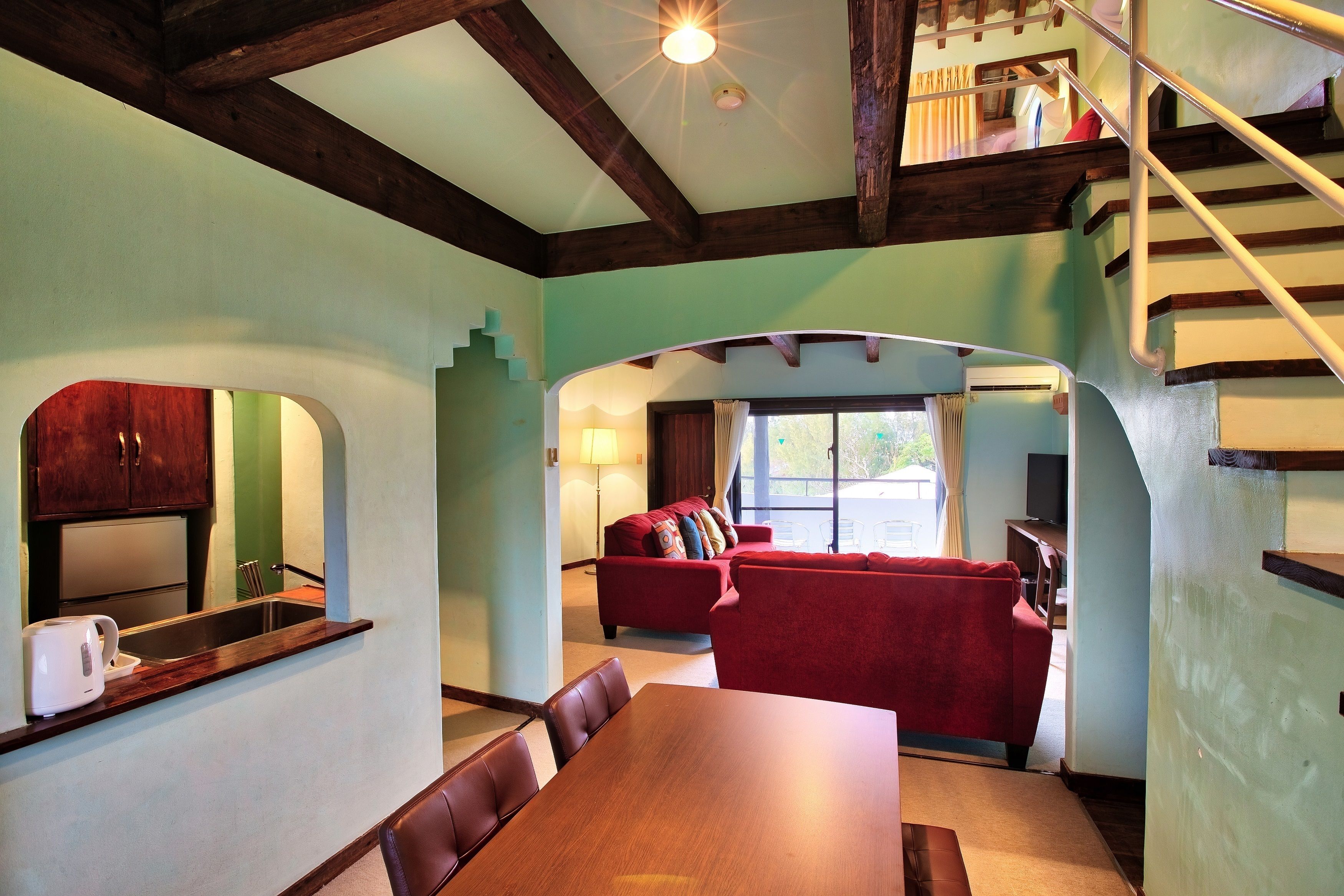 A dining area with a wooden table and chairs, a red sofa, and a kitchen with a sink and cabinets.