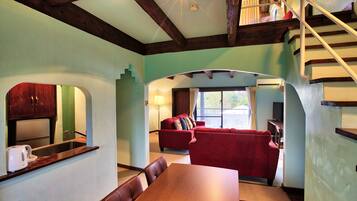 A dining area with a wooden table and chairs, a red sofa, and a kitchen with a sink and cabinets.