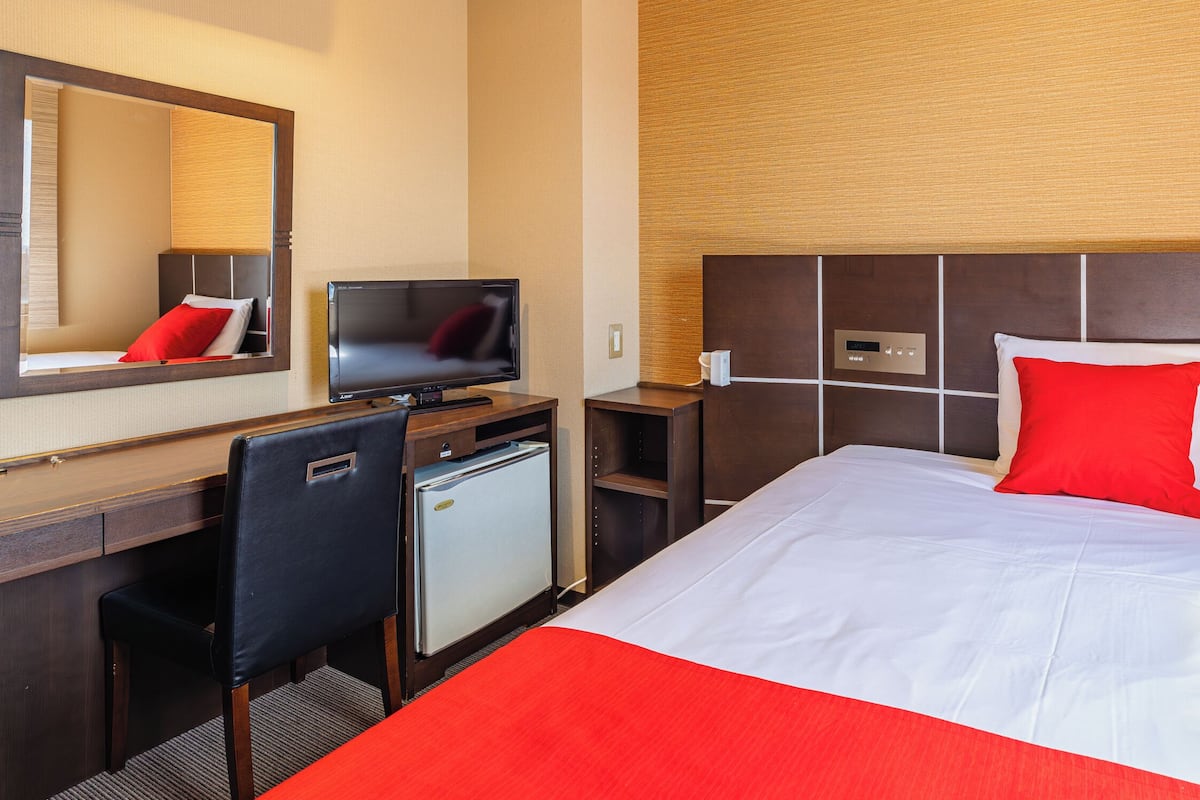 A hotel room with a bed, a desk, a chair, a television, and a small refrigerator.