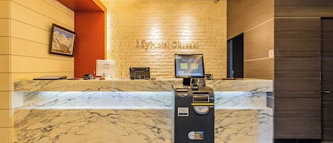 A hotel reception desk with a marble counter, a digital screen, and a self-service kiosk.