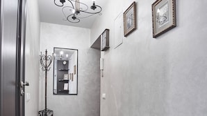 Ein Flur mit einem Kronleuchter, gerahmten Bildern an der Wand, einem Spiegel und einem weißen, zylindrischen Gegenstand.