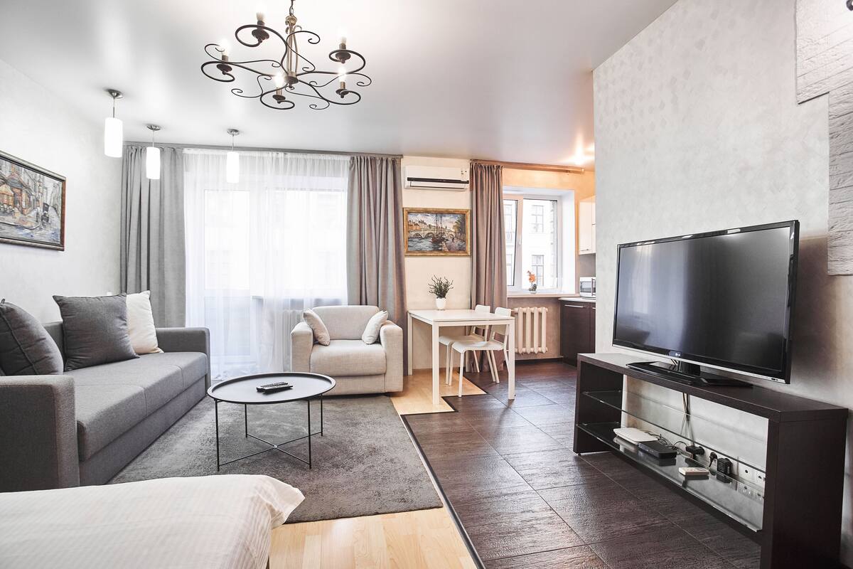 Una sala moderna con un sofá, una mesa de centro, un televisor y un comedor con una mesa y sillas.