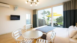 Una habitación de hotel con cama, televisión, mesa de comedor con sillas y un amplio ventanal con cortinas.