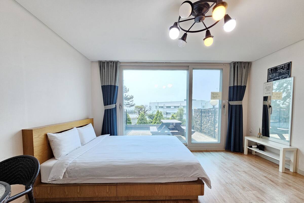 A modern hotel room with a large bed, wooden floor, and a balcony with curtains.