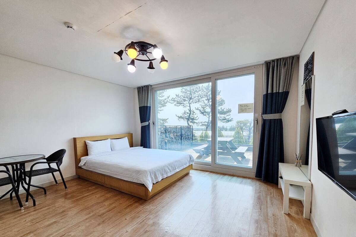 A hotel room with a bed, a desk, a chair, a TV, and a large window with a view of the outdoors.