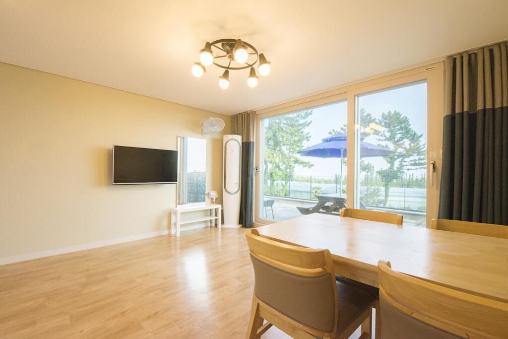 A spacious room with a large dining table, a flat-screen TV mounted on the wall, and a sliding glass door leading to an outdoor area.