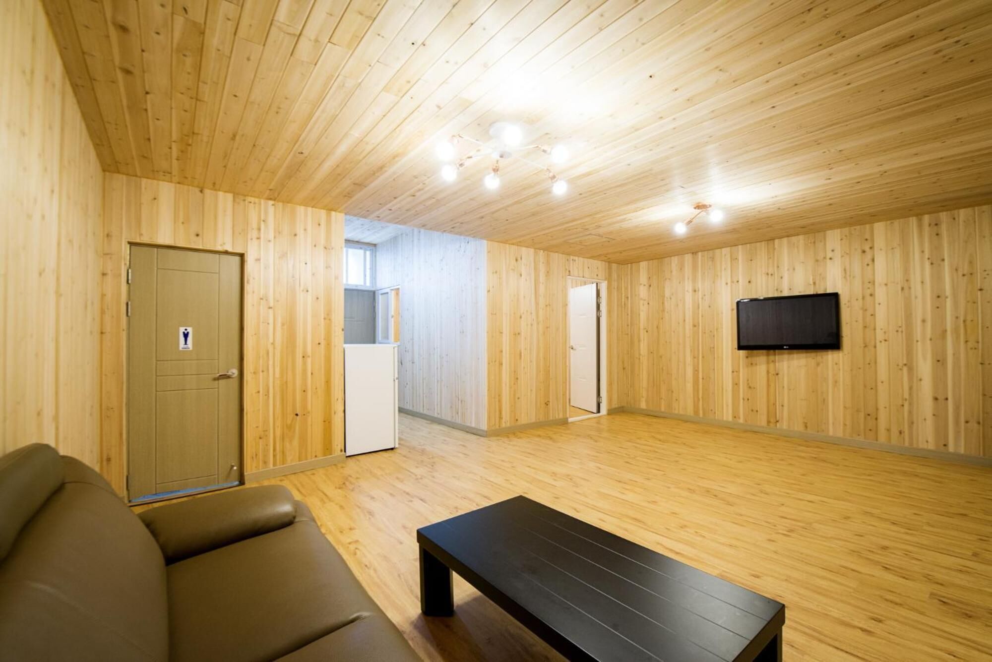 Une pièce aux murs et au plafond en bois, avec un canapé, un banc, un téléviseur et une porte ornée d’une icône.